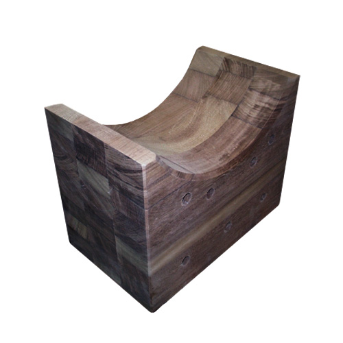 A wooden block with a smooth, curved groove carved into the top, and several round holes drilled into the side. The wood grain and blocky construction are visible.