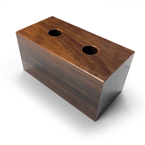 A rectangular wooden block with smooth finish and two circular holes on the top surface, placed on a white background.