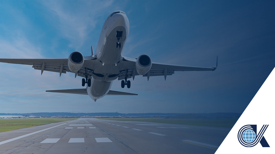 A commercial airplane takes off from a runway under a clear sky, with a blue gradient overlay and a circular globe logo in the bottom right corner.