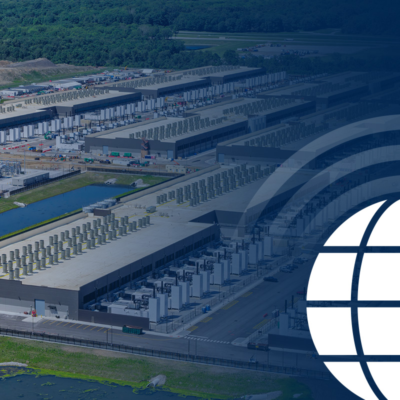 Aerial view of a large data center complex with multiple long buildings, cooling units, roads, and greenery. A stylized white globe graphic overlays the right side of the image.