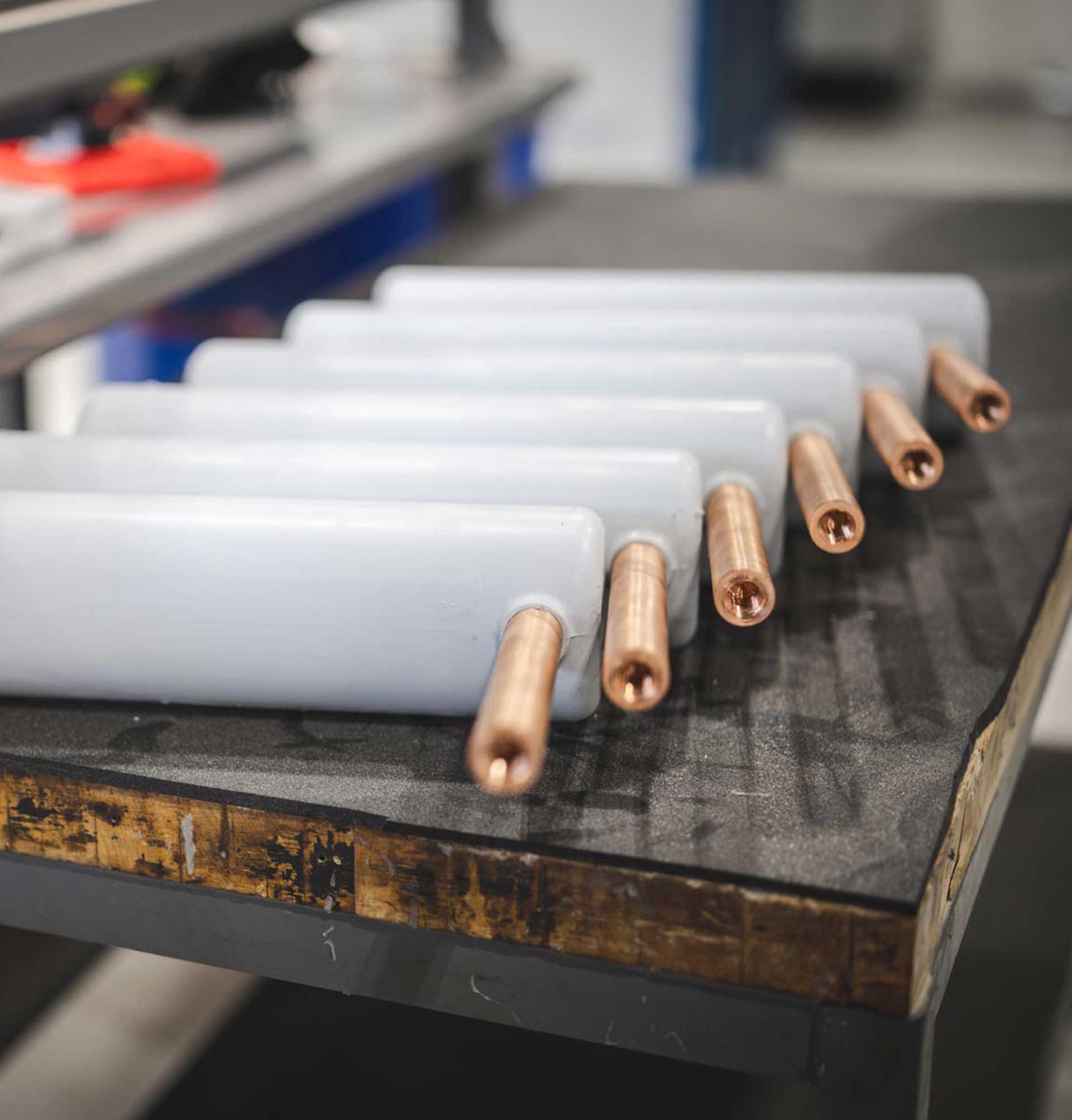 Several white rectangular objects with copper rods extending from one end are lined up on a padded workbench in an industrial or workshop setting.